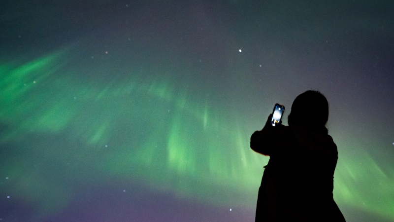 A person takes a photo of aurora borealis or the Northern Lights in Vancouver, B.C., Saturday, May. 11, 2024. THE CANADIAN PRESS/Ethan Cairns