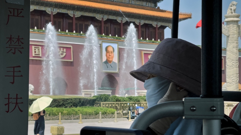 A woman wearing a hat and mask looks out from a bus travelling past Tienanmen Gate in Beijing, Monday, June 3, 2024. (AP Photo/Andy Wong) 