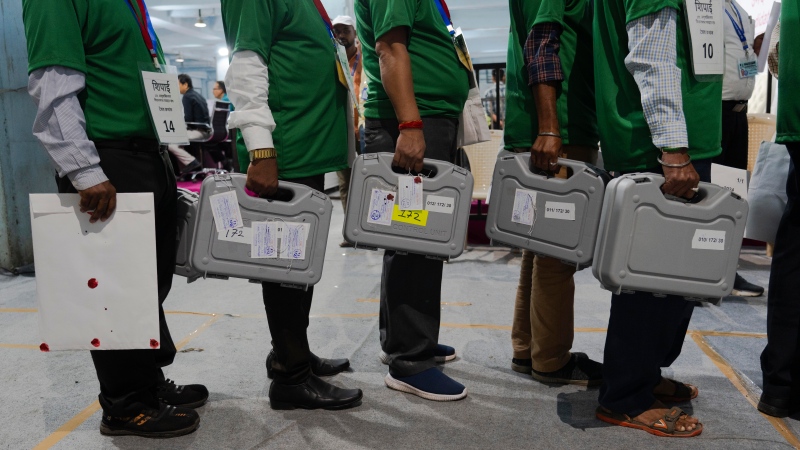 Election officials carry sealed electronic voting machines at a counting center in Mumbai, India, Tuesday, June 4, 2024.  (AP Photo/Rafiq Maqbool)