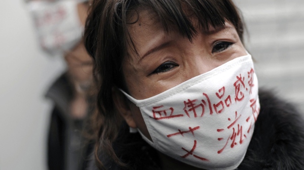In this file photo taken Dec. 1, 2009, a woman, whose son was infected with HIV, wears a face mask bearing the words "Blood products infect us with AIDS," as she cries during an AIDS awareness event on the World AIDS Day held at Beijing's south railway station. (AP Photo/Andy Wong)