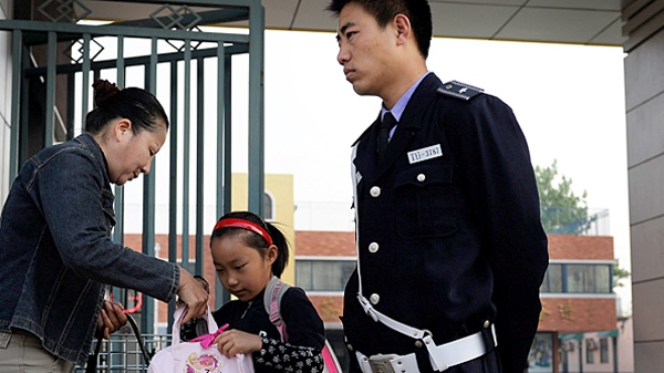 A woman helps her daughter while a security officer stands guard outside the Chijia Elementary School in Beijing, Tuesday, May 4, 2010. (AP / Andy Wong)