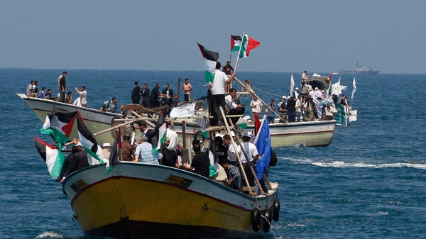 Palestinians ride boats in Gaza waters and an Israeli navy vessel patrols, background, as a flotilla of aid ships leaves for the blockaded territory, in Gaza city, Sunday, May 30, 2010. (AP / Hatem Moussa)