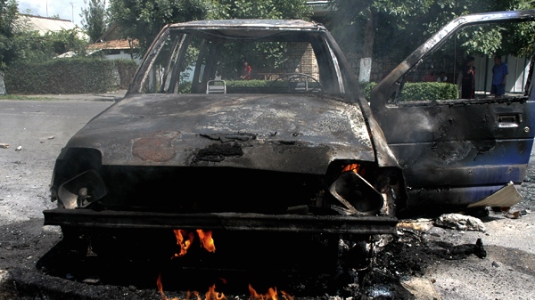 With a burning car in the foreground, a few local residents venture into a near empty street in Jalal-Abad, Kyrgyzstan, Sunday, June 13, 2010. (AP / Zarip Toroyev)