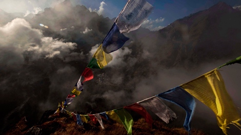 Tbetan Buddhist prayer flags flutter as thick cloud and fog roll over the area above Tengboche, center, in the Himalaya's Khumbu region, Nepal.(AP Photo/Kevin Frayer)