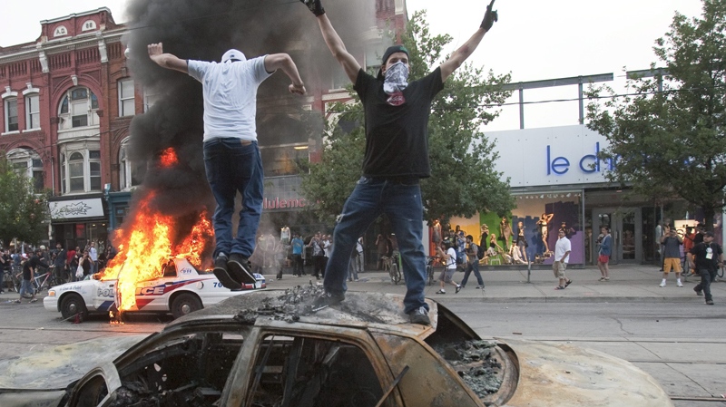 Protesters jump on a burnt-out police cruiser as a police car burns during on Queen Street West in Toronto, Saturday evening, June 26, 2010. (Ryan Remiorz / THE CANADIAN PRESS)