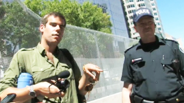 Charlie Veitchm, left, is seen speaking with a police officer in front of the G-20 summit security fence in Toronto. The 29-year-old filmmaker, was arrested Tuesday as he was about to board a plane at Toronto airport and charged of impersonating an officer.