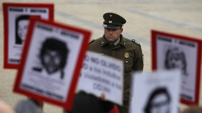 A police officer looks on as people hold portraits of family members who were dissidents killed during the dictatorship of former Gen. Augusto Pinochet outside La Moneda government palace in Santiago, Chile, Wednesday July 21, 2010. (AP Photo / Roberto Candia)