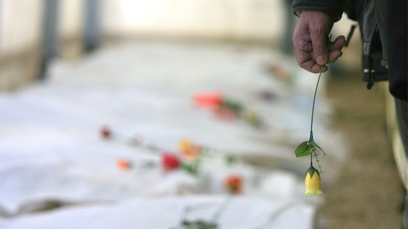 A Kosovo Albanian man holds a rose in his hand as he walks past the remains of 44 ethnic Albanians who were killed during Kosovo's 1998-99 war and buried in mass graves in Serbia after being brought back from Serbia and Montenegro in the border crossing of Merdare, Serbia-Montenegro, on Thursday, Dec.16, 2004. (AP / Visar Kryeziu)