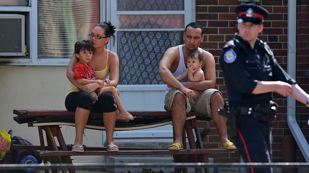 Neighbours watch on as police walk by on Tuesday July 17, 2012 near the scene of a shooting on Danzig Street where 19 people were injured and 2 confirmed dead at an outdoor barbecue that took place on Monday July 16, 2012 . (Aaron Vincent Elkaim / THE CANADIAN PRESS)
