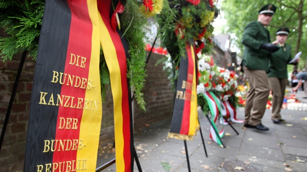 Police stand next to a wreath sent by German Chancellor Angela Merkel in front of the tunnel where 21 people died at the Love Parade techno music festival, in Duisburg, western Germany, Saturday, July 31, 2010. (AP / Michael Probst)
