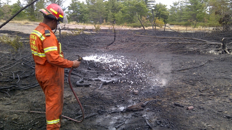 A firefighter puts out hot spots in a forest fire near Milford Bay, in the Muskoka Lakes region, on Wednesday, July 25, 2012. (Colin D'Mello/CTV)