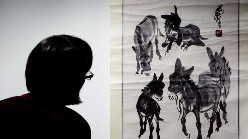 A woman looks at a fake painting of Chinese modern-artist Zhou Huang's 'Five Spirited Horses'.