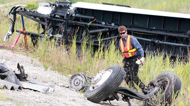 A tow truck operator looks at the front wheels that were sheared off, in the debris in at the scene of a coach bus accident on Highway 401 in Woodstock, Ontario, Sunday, August 22, 2010. (Dave Chidley / THE CANADIAN PRESS)