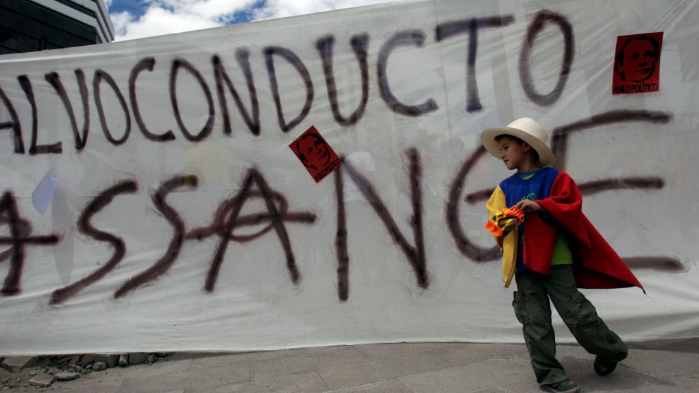 A child stands in front of a banner that reads in Spanish "Safe-conduct for Assange" during a demons