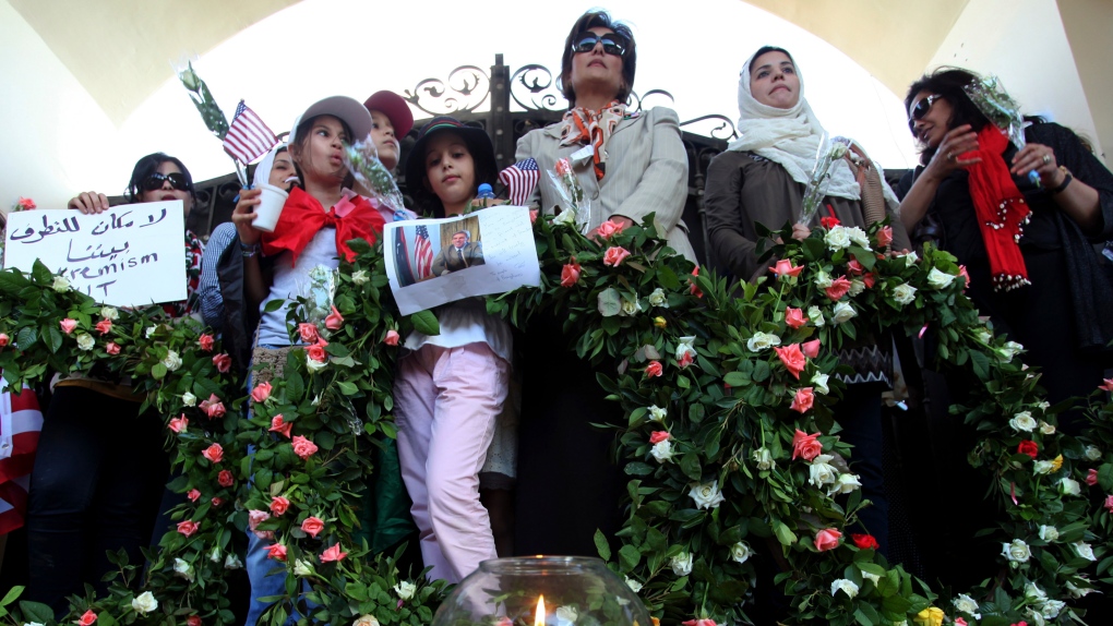 Libyans and Americans stand with wreaths, a poster and a photo of U.S. Ambassador Chris Stevens