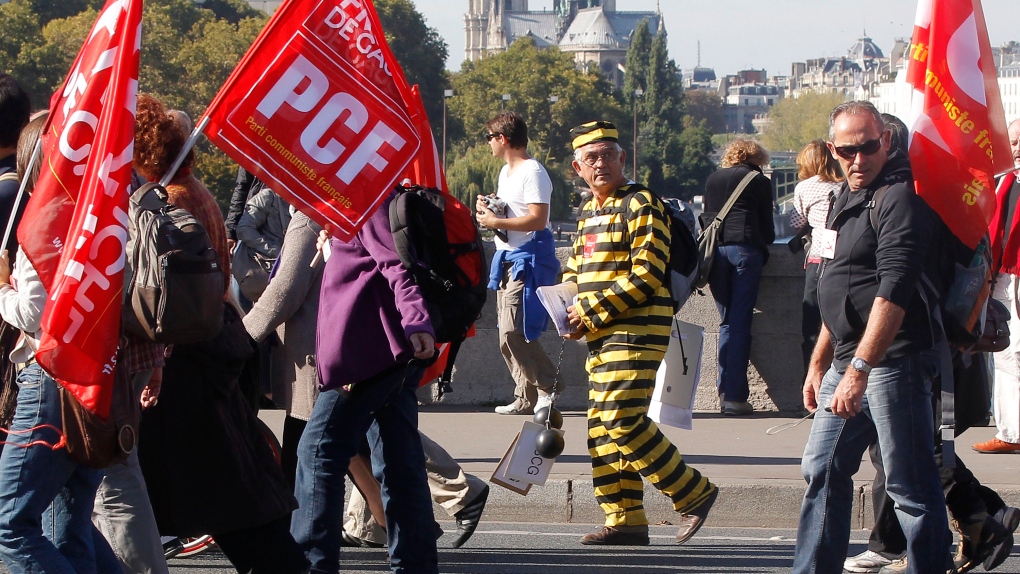 A demonstrator dressed like a prisoner marches between flags of the anti-capitalist party