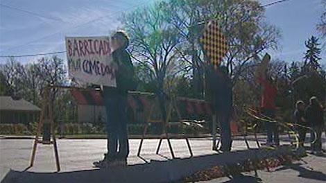 Residents hold up signs protesting a traffic barricade on Harrow Street.