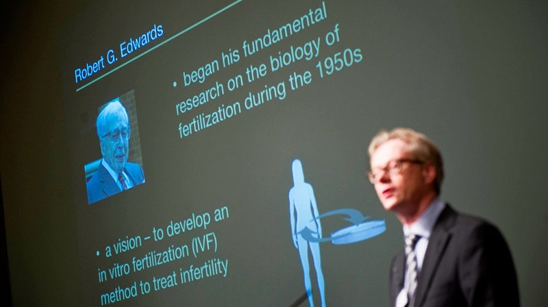 A picture of Robert Edwards of Britain is projected behind Christer Hoog of the Karolinska Institute as Hoog announces in Stockholm, Sweden, Monday Oct. 4 2010, that Edwards wins the 2010 Nobel Prize in medicine or physiology. (AP /Scanpix Sweden/Jessica Gow) 