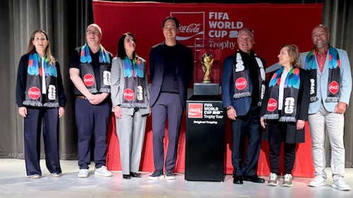 A group of people pose in a line for a picture with the FIFA World Cup Trophy.