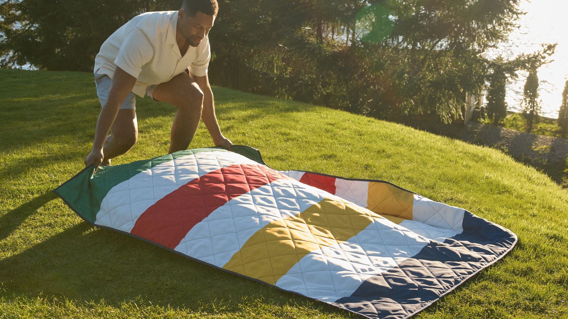 A person laying out a Canadian Tire Hudson's Bay striped blanket on a grassy lawn.
