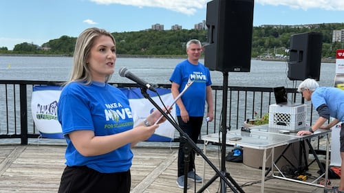 A woman wearing a blue t-shirt speaks into a microphone while holding a clipboard.