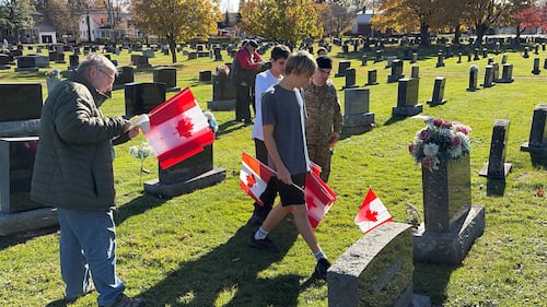 People place Canadian flags on gravesites.