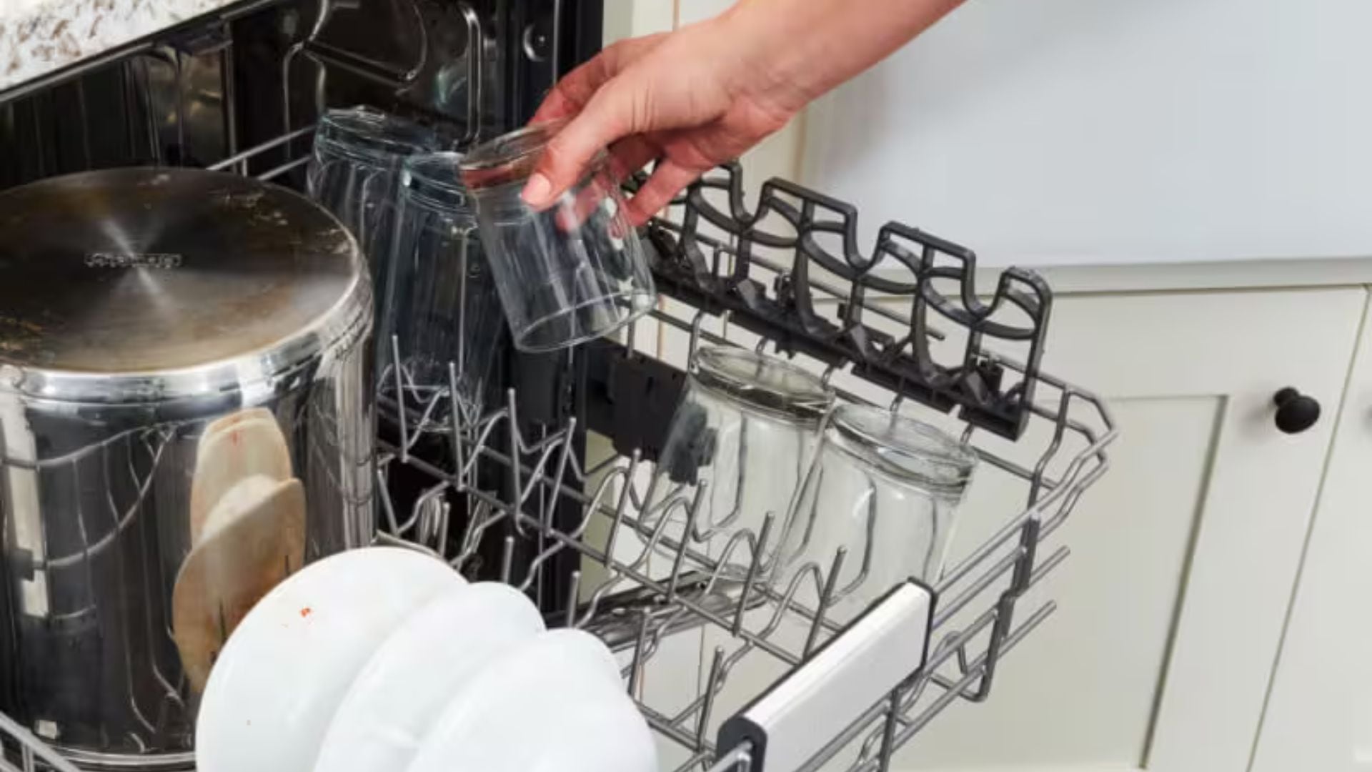 A person is putting a glass into a dishwasher.