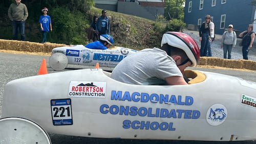 A soap box derby racer is pictured in a grey car.