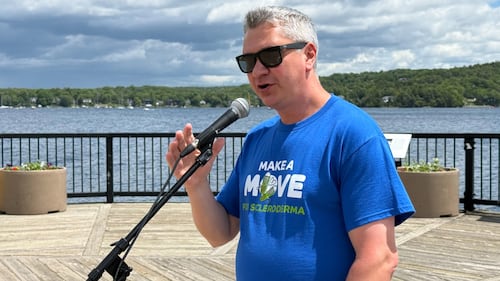 A man wearing a blue t-shirt speaks into a microphone.