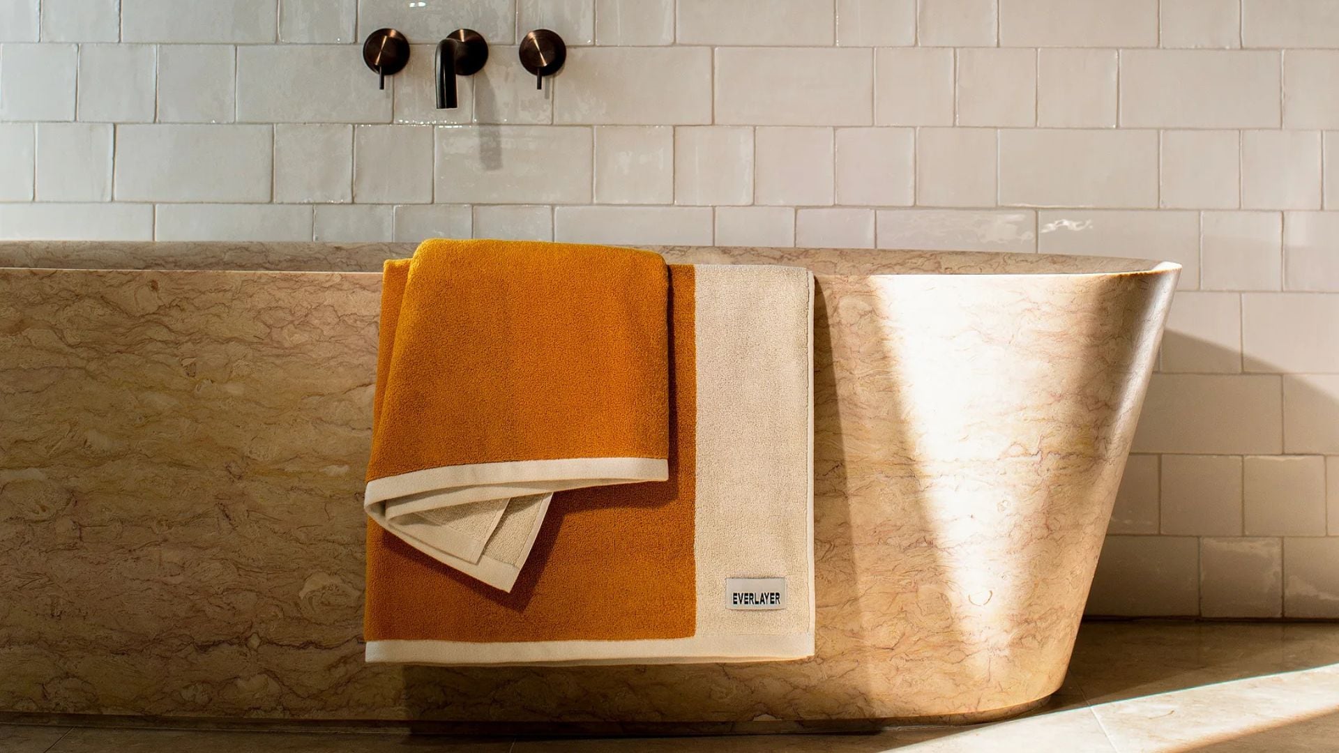 A bath towel on the edge of a marble tub.