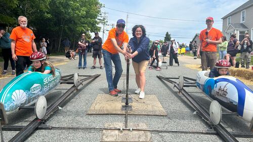 A man and woman pull a level to start a soap box derby race.