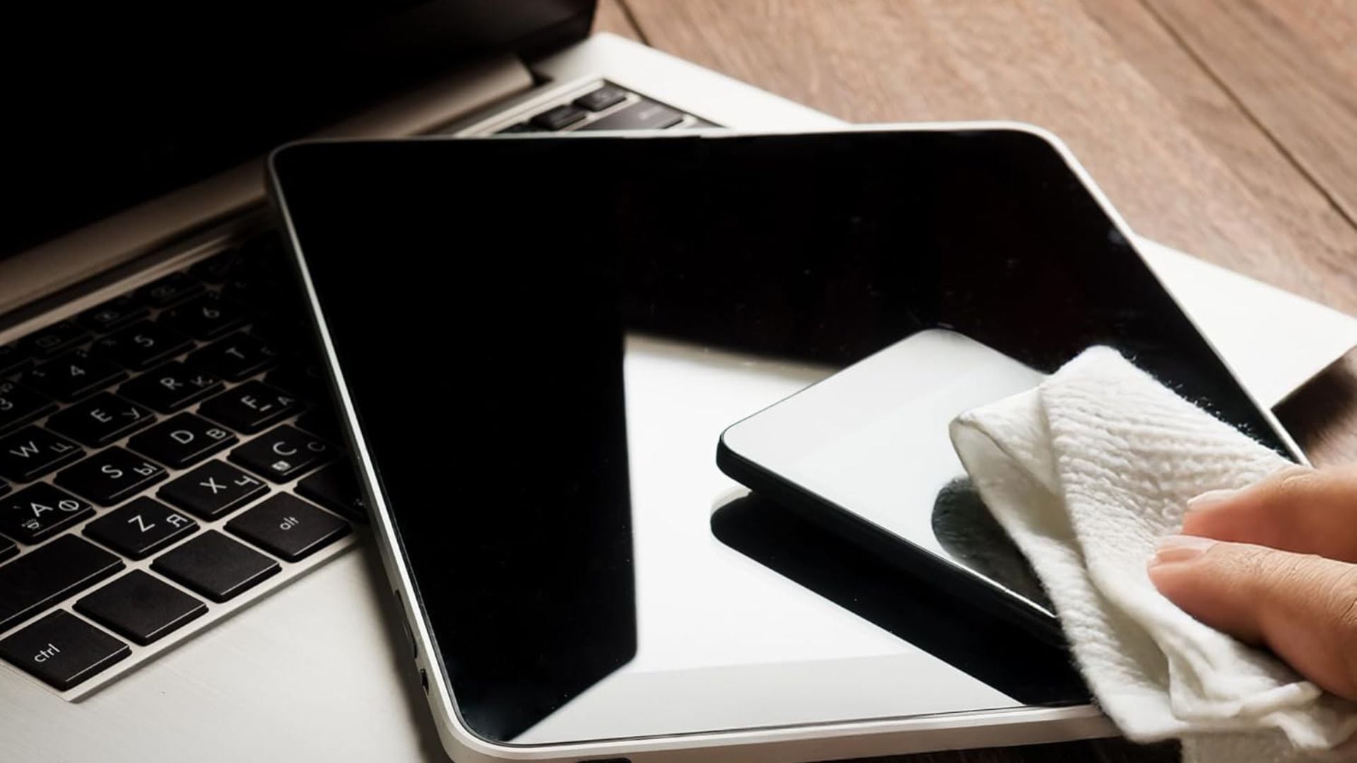 a person using wipes to clean the screen of a tablet that is sitting on top of a laptop