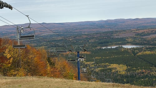 A ski lift is pictured with fall trees behind it.