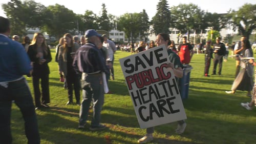 A woman holds a sign that reads "Save public health care" at the KDays pancake breakfast at the Alberta legislature on July 16, 2026. (Sean McClune / CTV News Edmonton)