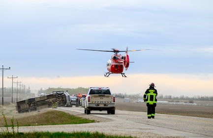 A STARS medical helicopter flies overhead as a fire fighter stands on Highway 672 near Beaverlodge, Alta., west of Grande Prairie, Alta., after a bus rollover resulted in several passengers being taken to hospital on Wednesday, May 13, 2026. THE CANADIAN PRESS/William Vavrek