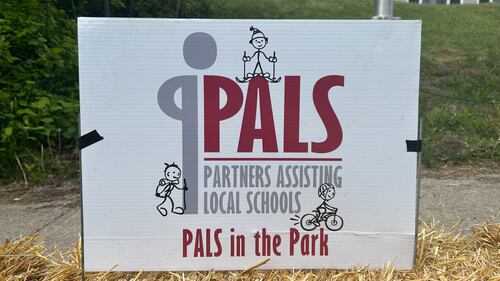 A white sign with red and grey writing is pictured reading "PALS: Partners Assisting Local Schools."