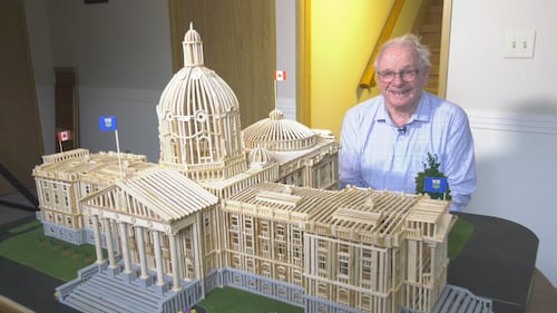 Esmond Warren poses for a picture with his miniature model of the Alberta legislature, which he built out of wood slivers over two winters, on April 14, 2026. (Evan Klippenstein / CTV News Edmonton)