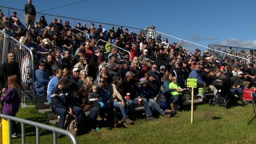 A crowd of people sit on bleachers.
