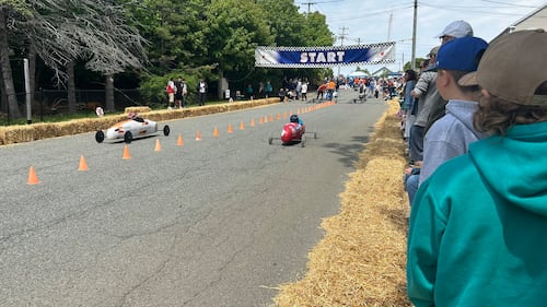 Soap box derby drivers race down a street.