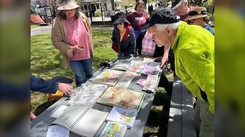 A group of people stand around a table of paintings.