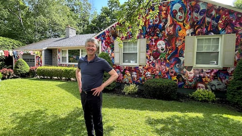 Artist Brian MacKinnon poses in front of his home, which is covered in painted faces, in Fredericton, N.B.