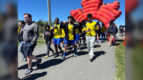 People wearing yellow jerseys walk in front of a large maple leaf.