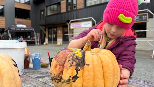 A girl wearing a pink hat paints a pumpkin.