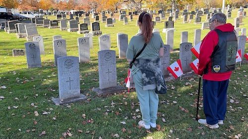 A man helps a girl place a Canadian flag on a grave.