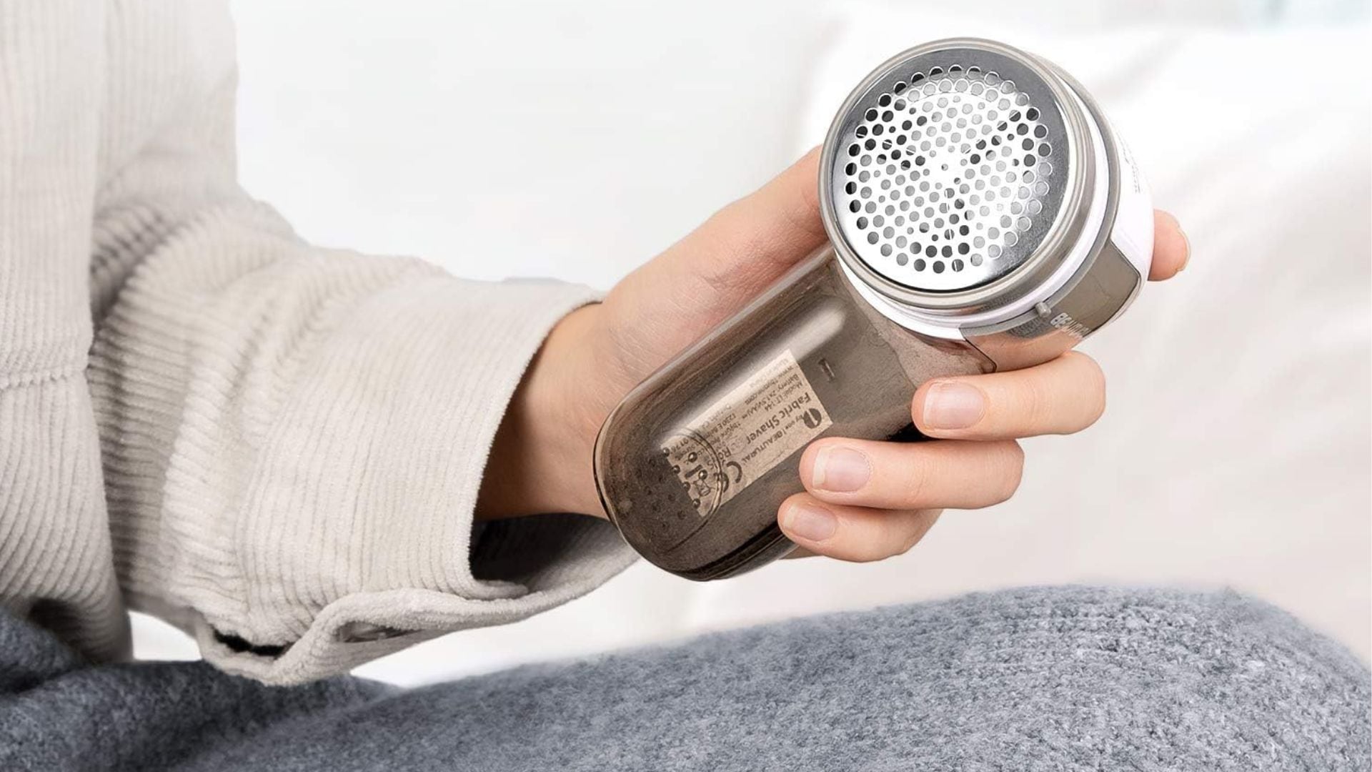 A person holding a BEAUTURAL Fabric Shaver over a sweater.