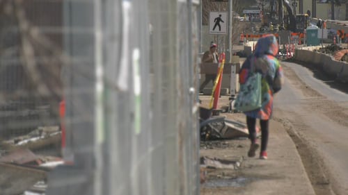 A pedestrian attempts to navigate the sidewalk along Stony Plain Road on April 1, 2026 as piles of debris from the Jasper Place Hotel encroach onto the pavement. (Galen McDougall/CTV News Edmonton)