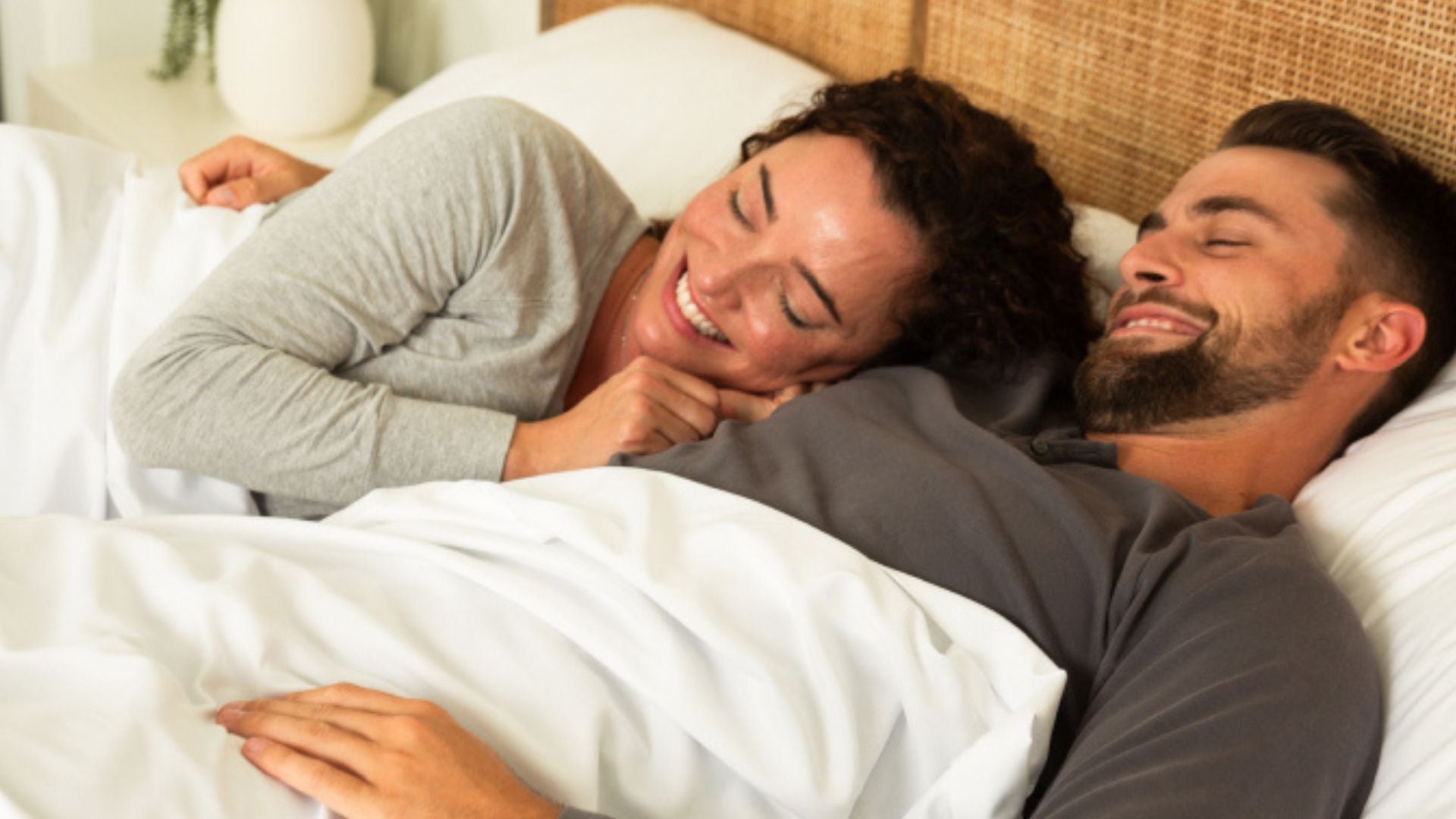 Two people lying in bed under CGK Unlimited sheets.