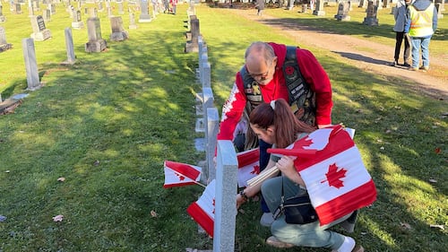 A man helps a girl place a Canadian flag on a grave.