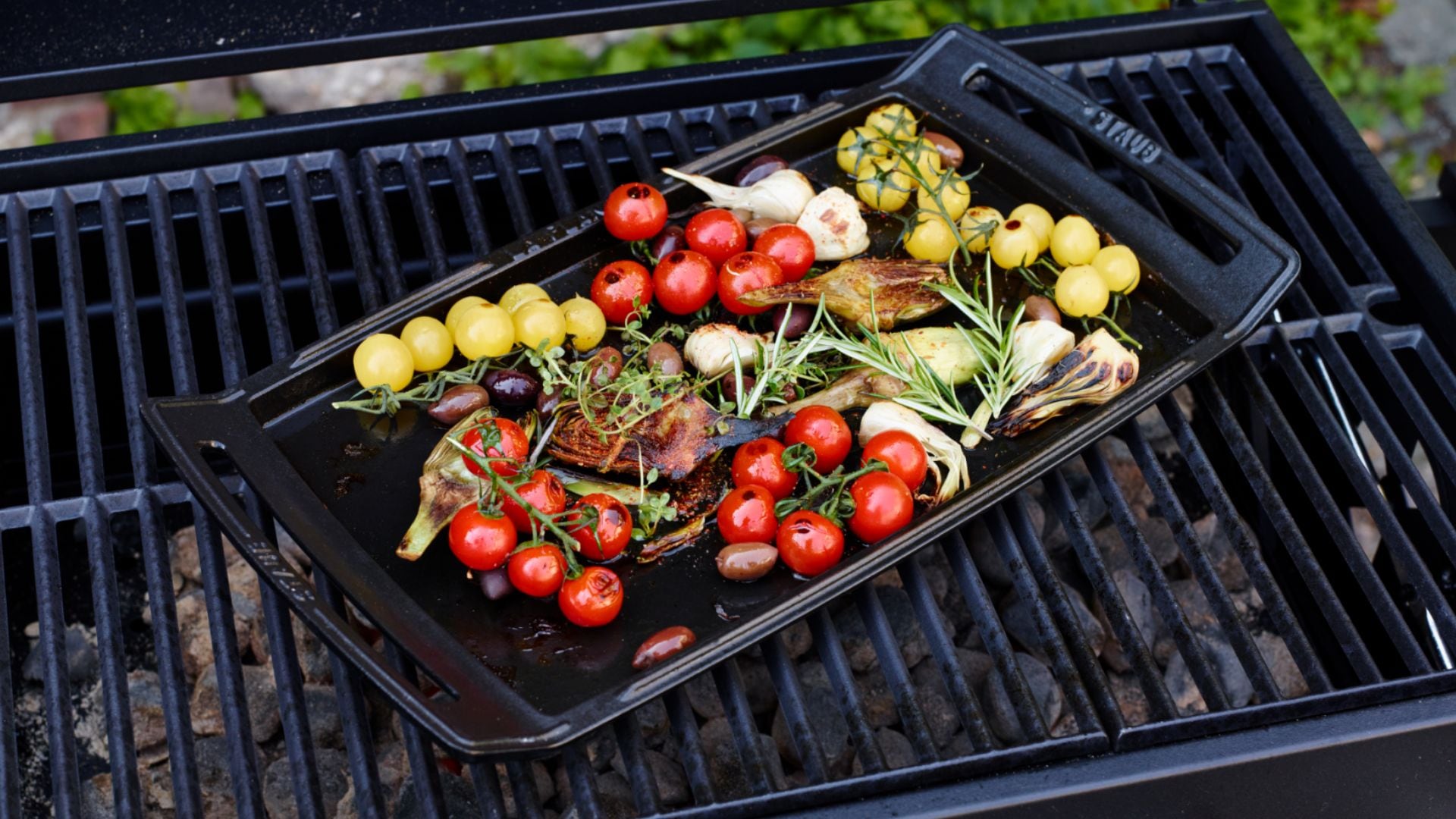 The STAUB La Plancha with veggies on it on top of a grill.