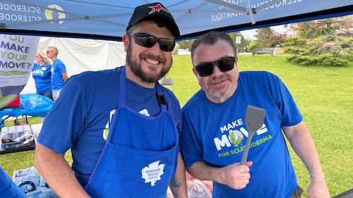 Two men wearing blue t-shirts pose for a photo at a barbecue.